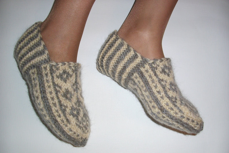 Puede incluir: Un par de zapatillas tejidas a mano con lana texturizada en tonos alternos de crema y gris carb&oacute;n. El dise&ntilde;o presenta un patr&oacute;n geom&eacute;trico de diamantes repetido en la parte superior y los lados, con detalles acanalados en el tal&oacute;n.