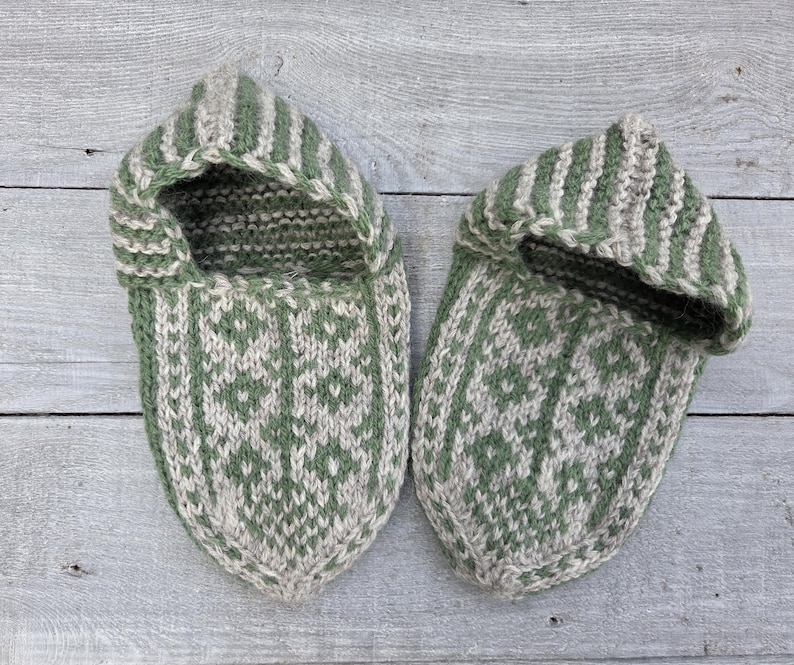 Puede incluir: Un par de zapatillas tejidas a mano con un dise&ntilde;o bicolor en verde salvia y beige avena. Las zapatillas presentan un patr&oacute;n geom&eacute;trico de rombos repetido en la parte superior, complementado con detalles de rayas verticales en el borde.