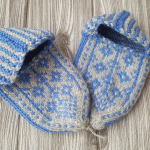 Puede incluir: Un par de zapatillas tejidas a mano con un esquema de color azul claro y beige. Las zapatillas muestran un patr&oacute;n geom&eacute;trico detallado en la puntera y el &aacute;rea del pie, con un dise&ntilde;o de pu&ntilde;o acanalado alrededor de la abertura, de hilo suave.