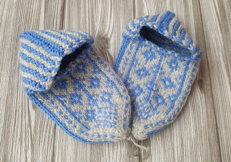 Puede incluir: Un par de zapatillas tejidas a mano con un esquema de color azul claro y beige. Las zapatillas muestran un patr&oacute;n geom&eacute;trico detallado en la puntera y el &aacute;rea del pie, con un dise&ntilde;o de pu&ntilde;o acanalado alrededor de la abertura, de hilo suave.