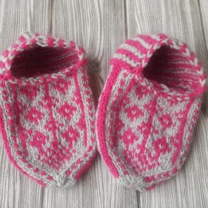 Puede incluir: Un par de zapatillas tejidas a mano con un vibrante patr&oacute;n geom&eacute;trico de diamantes en color rosa intenso y gris claro. Las zapatillas tienen un dise&ntilde;o de punta redondeada con un borde rosa intenso s&oacute;lido en la abertura y un pu&ntilde;o a rayas.