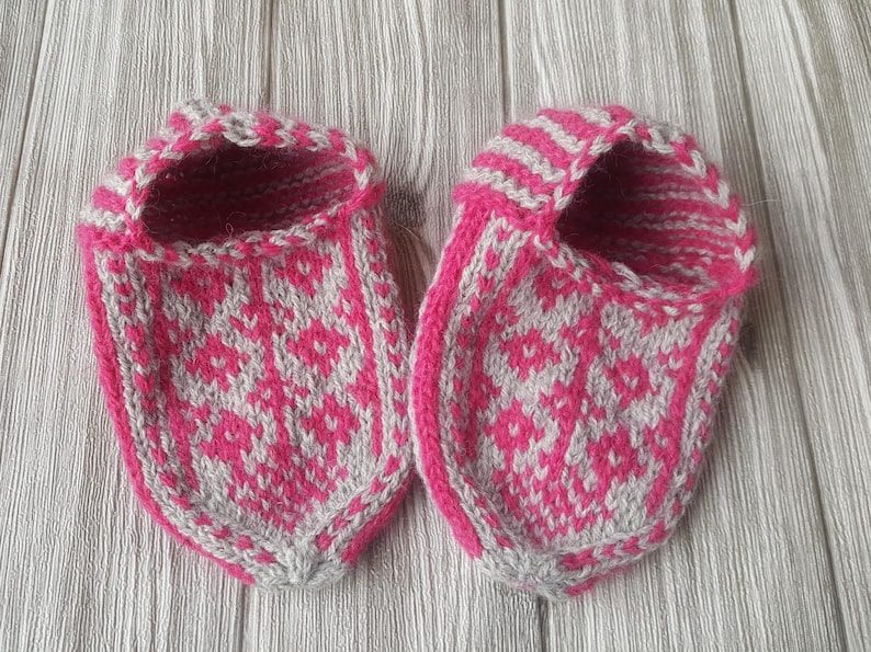 Puede incluir: Un par de zapatillas tejidas a mano con un vibrante patr&oacute;n geom&eacute;trico de diamantes en color rosa intenso y gris claro. Las zapatillas tienen un dise&ntilde;o de punta redondeada con un borde rosa intenso s&oacute;lido en la abertura y un pu&ntilde;o a rayas.