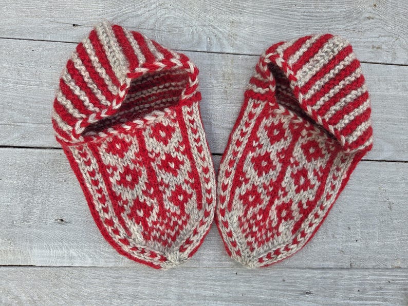 Puede incluir: Un par de zapatillas tejidas a mano con un dise&ntilde;o bicolor en rojo y beige. Las zapatillas presentan un patr&oacute;n floral geom&eacute;trico repetitivo en la parte superior y un dise&ntilde;o de rayas en el pu&ntilde;o, confeccionadas con hilo grueso y texturizado.