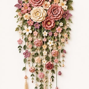 Puede incluir: Un tapiz de pared que presenta una colección de flores de ganchillo en tonos rosa empolvado, crema y malva, acentuadas con hojas de ganchillo verdes. El arreglo floral cuelga de un palo de madera horizontal con hilos colgantes.