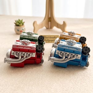 May include: A collection of miniature V-style engine models in red, blue, green, and yellow. Each engine features silver exhaust headers, a black circular component, and a valve cover with the text CISON ENGINES clearly visible on the side.