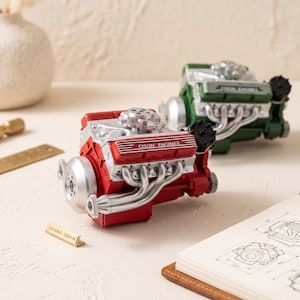 May include: Two 1:24 scale Cison V8 engine models, one red and one green, featuring silver exhaust manifolds and valve covers with the text CISON ENGINES. A small gold plaque reads 1:24 SCALE - CISON V8, accompanied by technical engine diagrams.
