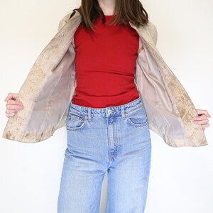 K&ouml;nnte beinhalten: Eine beige Wildlederjacke mit hellbraunem Futter. Die Jacke ist offen und das Futter ist sichtbar. Die Person, die die Jacke tr&auml;gt, tr&auml;gt auch ein rotes Tanktop und eine blaue Jeans.