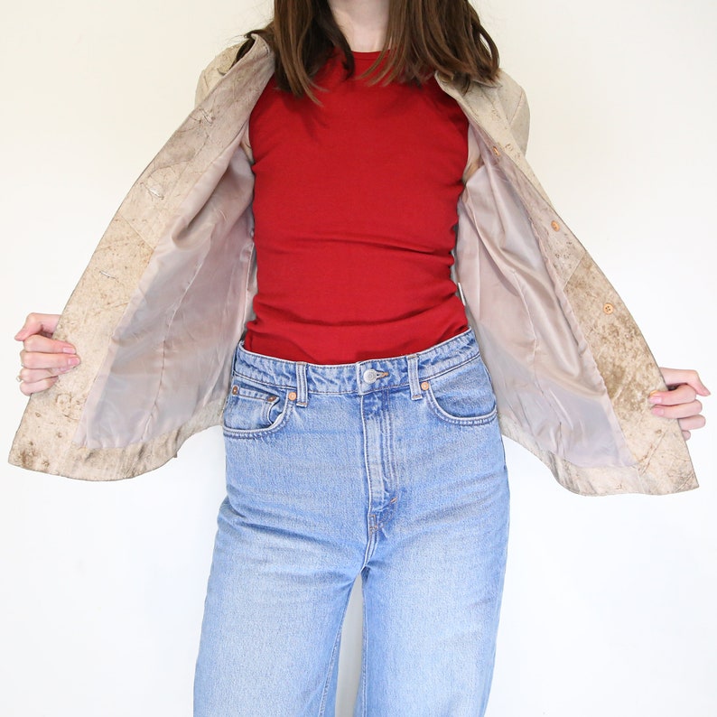 K&ouml;nnte beinhalten: Eine beige Wildlederjacke mit hellbraunem Futter. Die Jacke ist offen und das Futter ist sichtbar. Die Person, die die Jacke tr&auml;gt, tr&auml;gt auch ein rotes Tanktop und eine blaue Jeans.