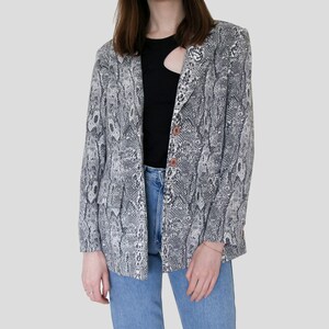 Könnte beinhalten: Ein grauer und weißer Blazer mit Schlangenhautmuster und einem einzigen Knopfverschluss.
