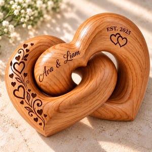 May include: Two interlocking wooden hearts with a natural grain finish. The left heart features an engraved vine pattern with small hearts. The right heart is engraved with the text Ava & Liam and EST. 2025 with two small hearts.