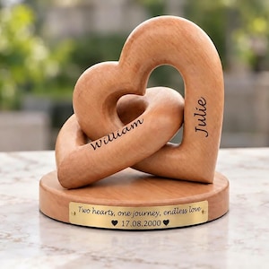 May include: A light brown wooden sculpture featuring two interlocking hearts mounted on a circular base. The name William is engraved on one heart, Julie on the other. A gold plaque reads: Two hearts, one journey, endless love, 17.08.2000.