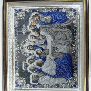 Op de afbeelding: Een ingelijst kunstwerk van kralen dat het Laatste Avondmaal voorstelt, met figuren in blauwe en zilveren gewaden met halo's. De rand is versierd met blauwe en heldere kristallen en witte parels. Cyrillische tekst is links zichtbaar.