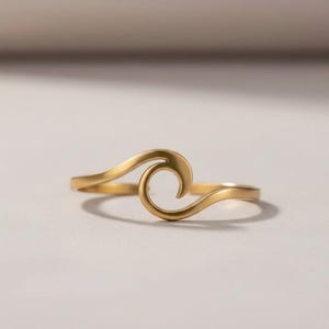 Könnte beinhalten: Ein goldfarbener Ring mit einem durchgehenden, fließenden wellenförmigen Design, das sich zu einer zentralen Spirale krümmt. Das Band ist vorne offen und weist eine glatte, polierte metallische Oberfläche auf, die das Licht reflektiert.
