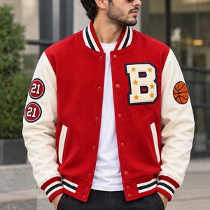 May include: A red and cream varsity jacket featuring a large letter B with yellow stars on the chest, two circular patches with the number 21 on the right sleeve, and a basketball graphic on the left sleeve. It has a snap-button front closure.