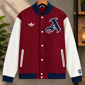 Puede incluir: Una chaqueta universitaria de color granate con mangas blancas y cuello, puños y dobladillo de canalé azul oscuro. La parte delantera presenta un logotipo de trébol de Adidas blanco, un gran parche con la letra A azul marino y botones.