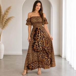 Op de afbeelding: Een off-shoulder maxi-jurk met een bruin en zwart luipaardpatroon. Het lijfje is gesmokt en de korte mouwen zijn voorzien van ruches. De rok toont een groot, opvallend vlindergrafisch ontwerp in een bijpassende luipaardprint.