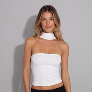 Op de afbeelding: Een witte strapless tube top met een bijpassend losse choker-halsband. Het kledingstuk is gemaakt van effen witte stof met een nauwsluitend silhouet dat van de borst tot aan de taille loopt, gecombineerd met een losse hoge halsband.