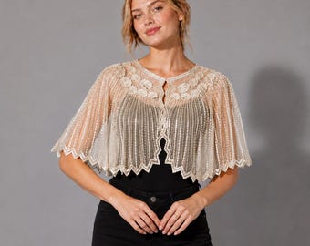 May include: A sheer, champagne-colored bolero capelet featuring intricate vertical beaded stripes and a scalloped hemline. The garment has a rounded neckline adorned with floral-shaped embroidery and sequins, worn over a solid black top.