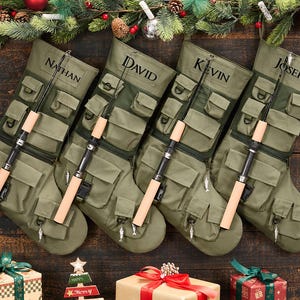 Peut inclure: Quatre chaussettes de Noël tactiques vert olive dotées de multiples poches utilitaires, d'anneaux en D et d'une canne à pêche miniature fixée sur le devant. Chaque chaussette est personnalisée avec les noms Nathan, David, Kevin et Joseph en noir.