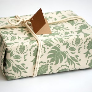 May include: A gift wrapped in white paper with a green floral pattern. The gift is tied with twine and has a brown paper tag.