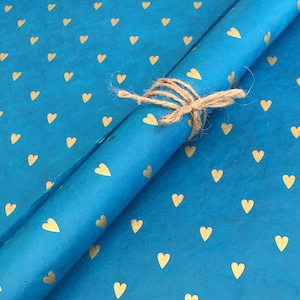 May include: Blue wrapping paper with a gold heart pattern. The paper is rolled up and tied with twine.
