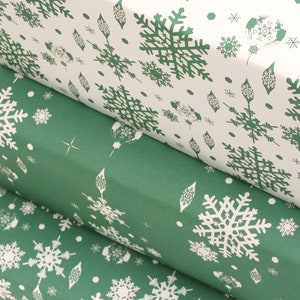 K&ouml;nnte beinhalten: Nahaufnahme von drei Geschenkpapierrollen. Die obere Rolle ist wei&szlig; mit einem gr&uuml;nen Schneeflockenmuster. Die mittleren und unteren Rollen sind gr&uuml;n mit einem wei&szlig;en Schneeflockenmuster. Das Papier ist aufgerollt und zeigt das Muster an den R&auml;ndern.