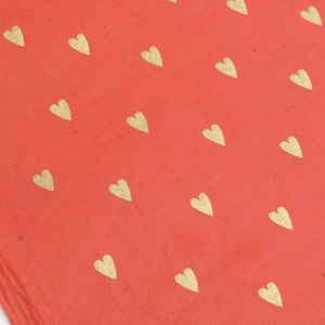 May include: Red wrapping paper with a repeating pattern of gold hearts.
