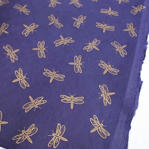 May include: A deep purple fabric with a repeating pattern of gold dragonfly silhouettes.