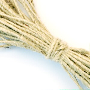 May include: A close-up of a bundle of natural twine, a type of string made from plant fibers, tied together in a knot. The twine is a light beige color and has a rough texture.