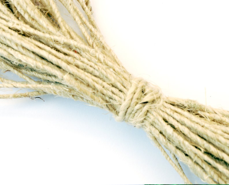 May include: A close-up of a bundle of natural twine, a type of string made from plant fibers, tied together in a knot. The twine is a light beige color and has a rough texture.