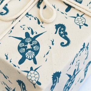 May include: A white gift wrap with a blue seahorse, turtle, and fish pattern. The wrapping paper is tied with a white twine bow.