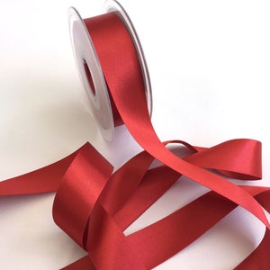 May include: A spool of red satin ribbon with a few loops of ribbon unraveled from the spool.