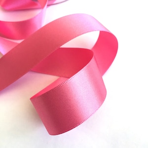 May include: A pink satin ribbon, curled and twisted, against a white background.