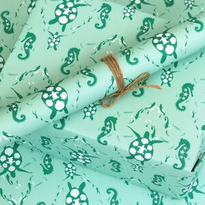 May include: Two rolls of teal blue wrapping paper with a repeating pattern of seahorses and sea turtles. The paper is tied together with twine.