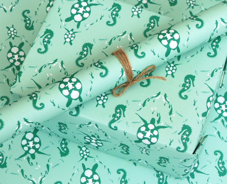 May include: Two rolls of teal blue wrapping paper with a repeating pattern of seahorses and sea turtles. The paper is tied together with twine.