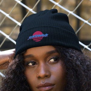 Classic organic cotton ribbed beanie. Synthwave in retro front in bright blue with hot pink shadow over a sunset in hot pink.
6 colours available.
Oxford Navy
Black
Light Avio Blue
Light Grey
Leaf Green
Mustard Yellow.
Model wears oxford navy with pale mustard shirt and jeans.