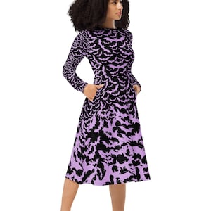 Bats dress. Long sleeves. Midi length (below the knee). Flared skirt. Pockets. Black base with bats of varying sizes in pastel purple (lilac) forming an all over pattern. The skirt has larger bats overlapping each other. Front left hand in pockets.