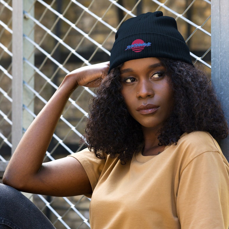 Classic organic cotton ribbed beanie. Synthwave in retro front in bright blue with hot pink shadow over a sunset in hot pink.
6 colours available.
Oxford Navy
Black
Light Avio Blue
Light Grey
Leaf Green
Mustard Yellow.
Model wears oxford navy with pale mustard shirt and jeans.