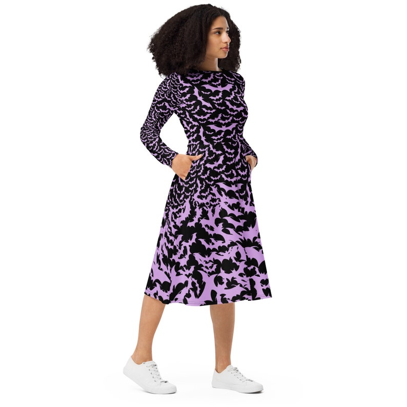 Bats dress. Long sleeves. Midi length (below the knee). Flared skirt. Pockets. Black base with bats of varying sizes in pastel purple (lilac) forming an all over pattern. The skirt has larger bats overlapping each other. Front left hand in pockets.