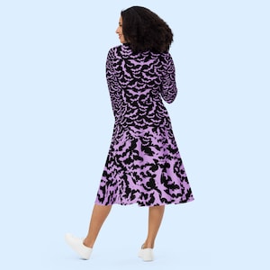Bats dress. Long sleeves. Midi length (below the knee). Flared skirt. Pockets. Black base with bats of varying sizes in pastel purple (lilac) forming an all over pattern. The skirt has larger bats overlapping each other. Facing back.