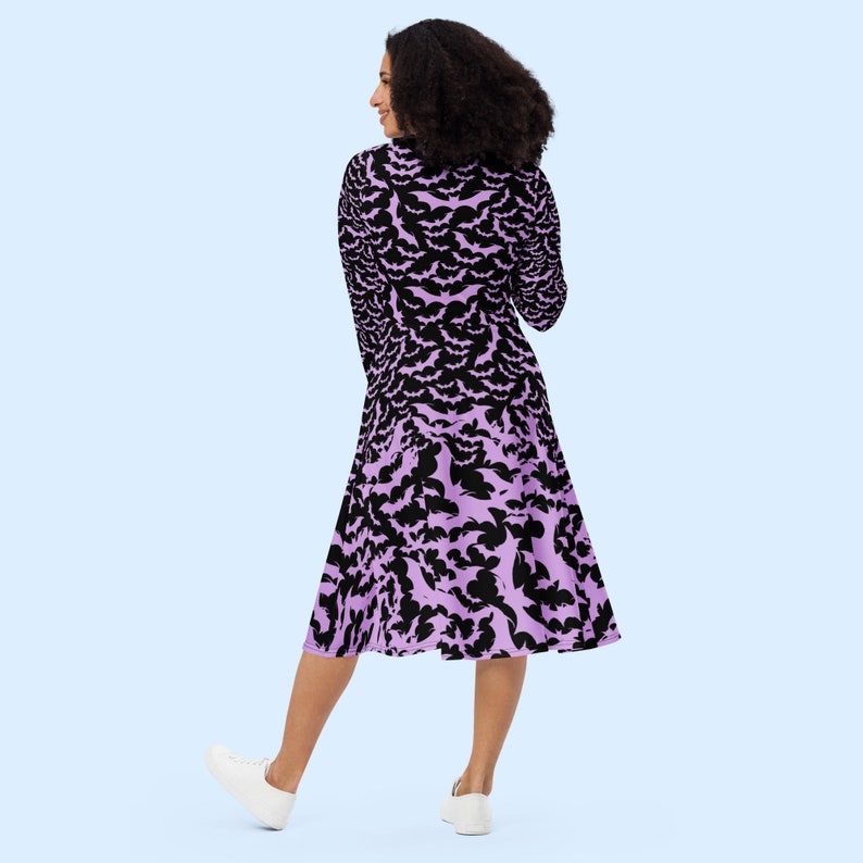 Bats dress. Long sleeves. Midi length (below the knee). Flared skirt. Pockets. Black base with bats of varying sizes in pastel purple (lilac) forming an all over pattern. The skirt has larger bats overlapping each other. Facing back.