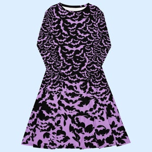 Bats dress. Long sleeves. Midi length (below the knee). Flared skirt. Pockets. Black base with bats of varying sizes in pastel purple (lilac) forming an all over pattern. The skirt has larger bats overlapping each other. Front flat.