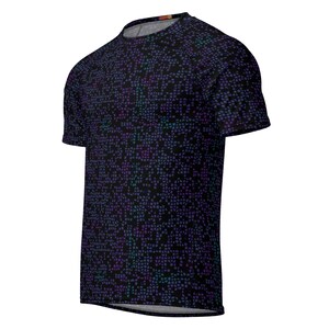 May include: A short-sleeved t-shirt with a dark background and a repeating pattern of small, irregular shapes in shades of purple and teal. The shirt has a crew neck and a slightly curved hemline.