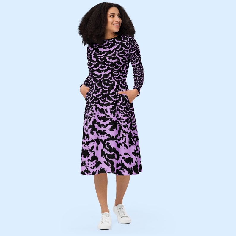 Bats dress. Long sleeves. Midi length (below the knee). Flared skirt. Pockets. Black base with bats of varying sizes in pastel purple (lilac) forming an all over pattern. The skirt has larger bats overlapping each other. Front hand in pockets.