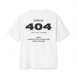 May include: A white short-sleeved t-shirt featuring black text that reads ERROR 404 LOVE NOT FOUND, followed by SORRY! CURRENTLY BUSY LOOKING FOR MONEY, NOT LOVE. The design is centered on the back of the garment with a clean, minimalist aesthetic.