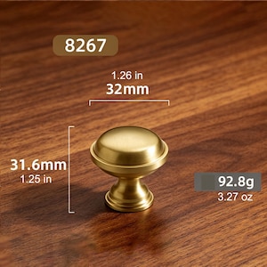 May include: A gold-toned metal cabinet knob with a smooth, rounded top and a tapered base. The knob is labeled with the number 8267 and has a diameter of 1.26 inches, a height of 1.25 inches, and a weight of 3.27 ounces as indicated in the image.