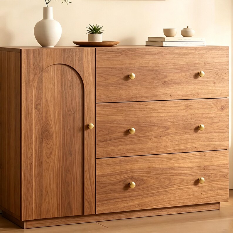 May include: A wooden cabinet with a light brown wood grain finish, featuring one vertical door with an arched panel design and three horizontal drawers. Each drawer and the door are equipped with a small, round, brushed gold metal knob.
