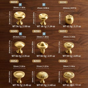 May include: A collection of nine gold-toned metal cabinet knobs in various shapes, including round, apple-shaped, and ribbed designs. Each knob is labeled with a model number, dimensions in inches, and weight in ounces, ranging from 0.98 to 1.38 inches.