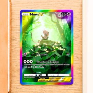 May include: A Mew ex trading card featuring a rainbow holographic border and a full-art illustration of the pink Mew character sitting on a pile of green stone blocks in a forest. The card displays 130 HP, Psyshot and Genome Hacking attacks.