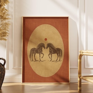 May include: A rectangular wall art print featuring a dark brown illustration of two horses facing each other inside a large, centered beige oval. A small, solid dark red circle is positioned above the horses, set against a deep terracotta background.